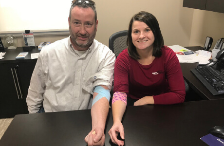 Two employees showing their arms with a bandage after donating blood for the nebraska community blood bank