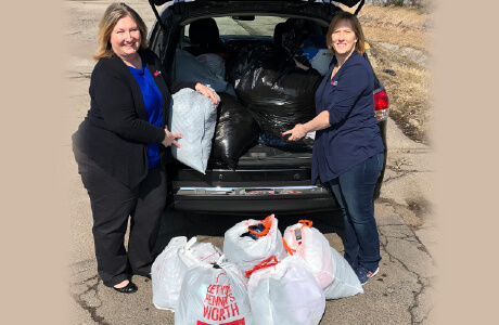 Two employees standing behind a car filled with bags of clothes to be donated