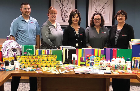 A group of employees standing behind stacks of school supplies to be donated