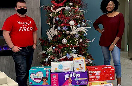 A group of employees standing behind boxes of diapers to be donated to the lydia house