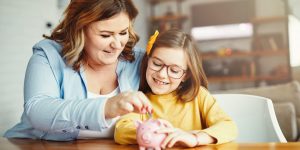mother and daughter putting coins in a piggy bank at home